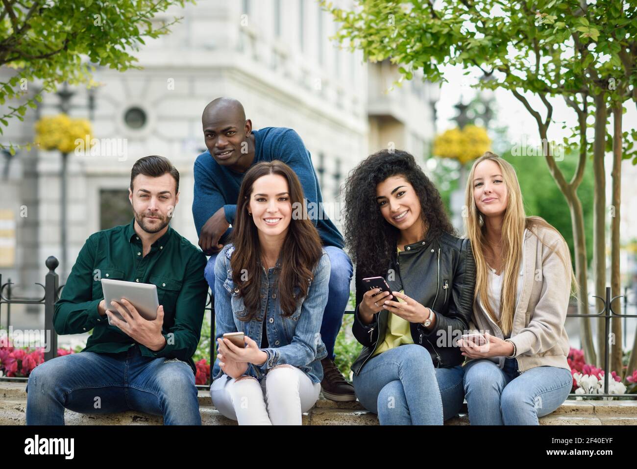 Multi-ethnischen Gruppe junger Menschen mit Smartphones und Tablet Pcs im Freien im städtischen Hintergrund. Frauen und Männer Lächeln und Lachen in der Straße legere Kleidung. Stockfoto