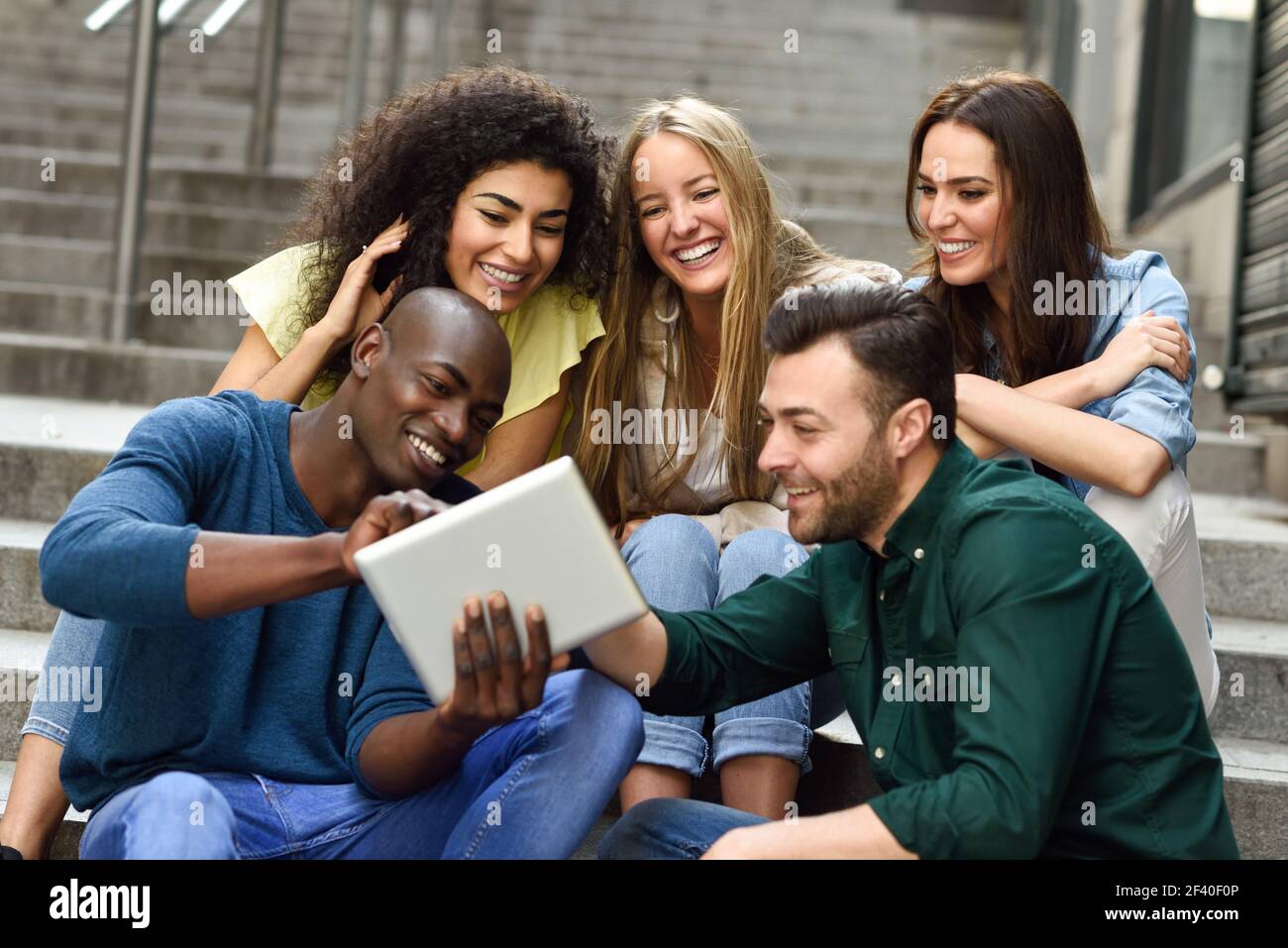 Multi-ethnischen Gruppe junger Menschen auf einen Tablet-PC im Freien im städtischen Hintergrund. Gruppe Männer und eine Frau sitzen gemeinsam über Schritte. Stockfoto