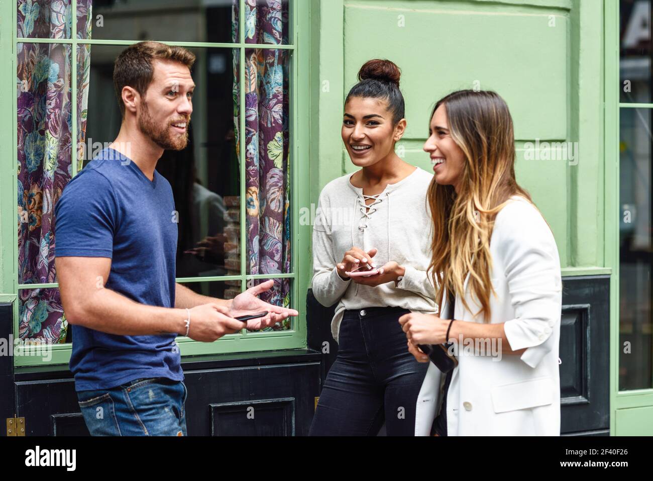 Drei multiethnischen Menschen reden und lächeln im Freien mit smart phone in ihren Händen. Multiethnische Gruppe von Freunden im städtischen Hintergrund. Stockfoto