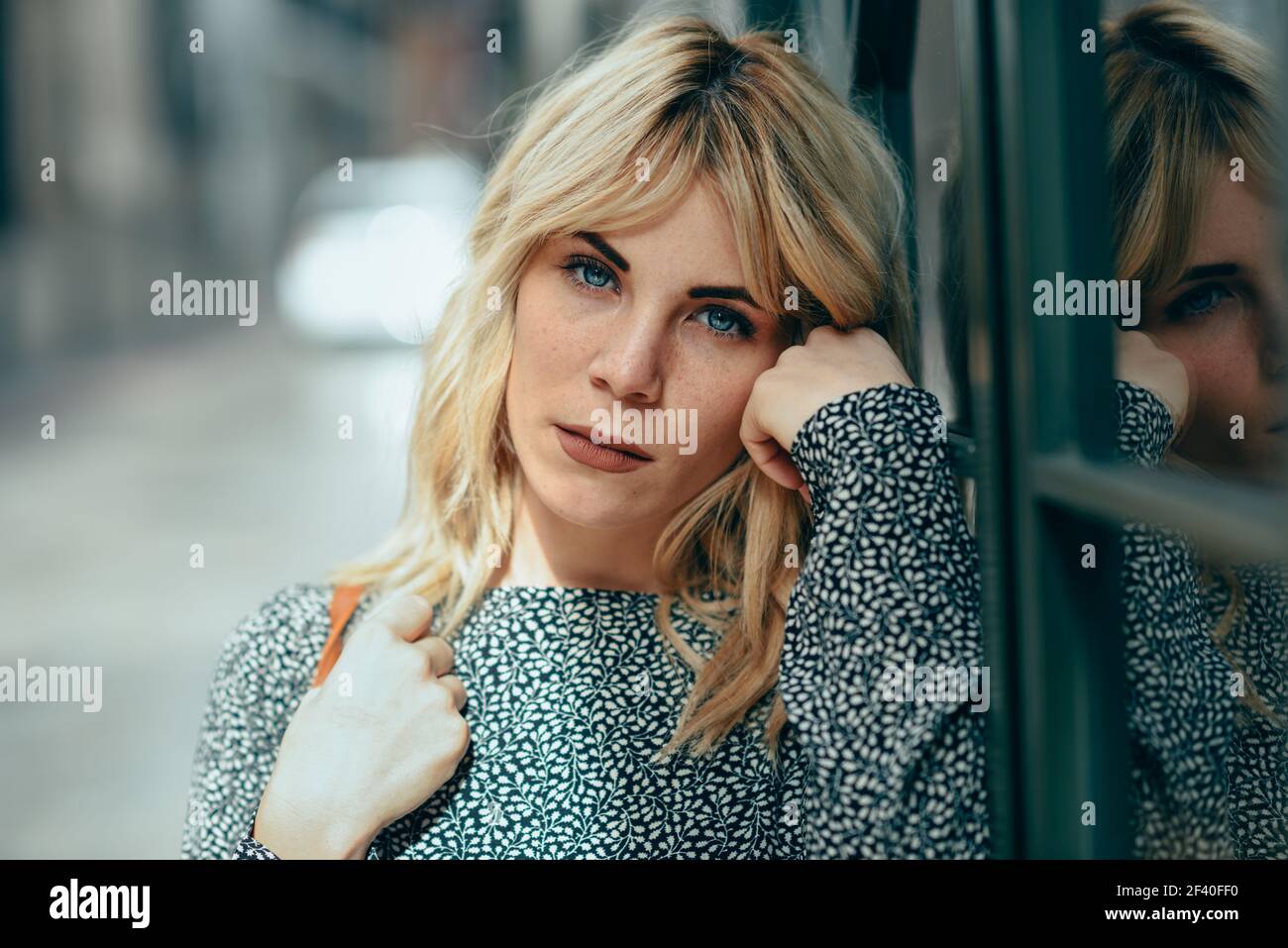 Porträt von Ernst junge blonde Frau, die auf den städtischen Hintergrund. Schöne Mädchen mit blauen Augen tragen Kleid stehen im Freien. Stockfoto