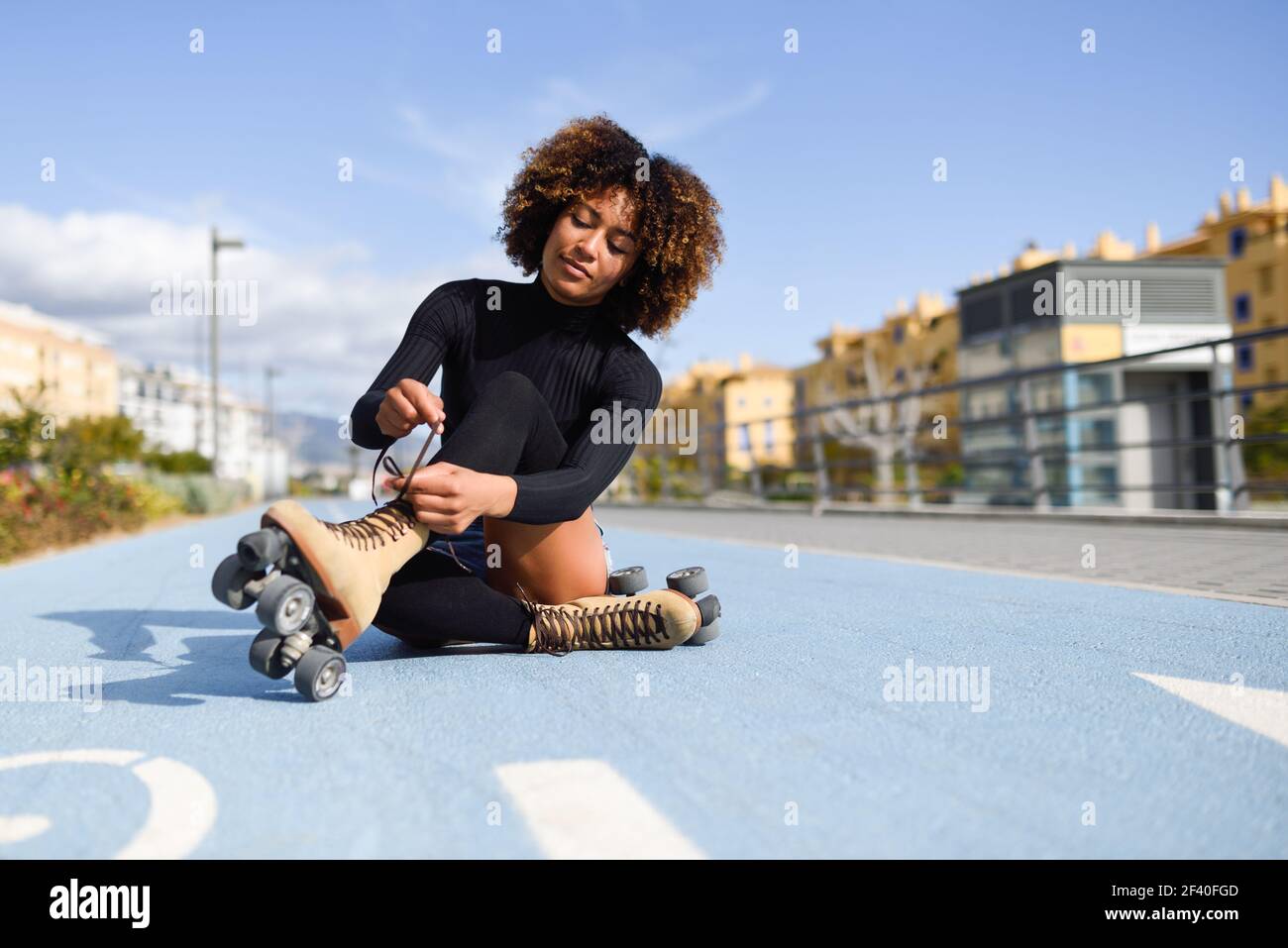 Junge lächelnde schwarze Mädchen sitzen auf dem Fahrrad Linie und setzt auf den Skates. Frau mit Afro Frisur rollerblading an einem sonnigen Tag Stockfoto