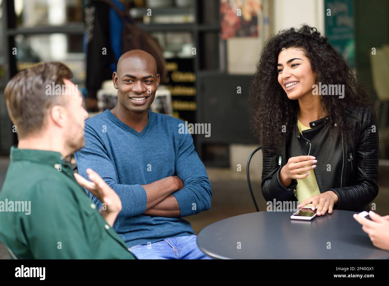 Multirassische Gruppe von Freunden warten auf einen Kaffee zusammen. Zwei Männer und ein Mann sitzen im Café, reden und lächeln. Lifestyle- und Freundschaftskonzepte mit echten Menschen-Modellen. Multirassische Gruppe von Freunden warten auf einen Kaffee zusammen Stockfoto