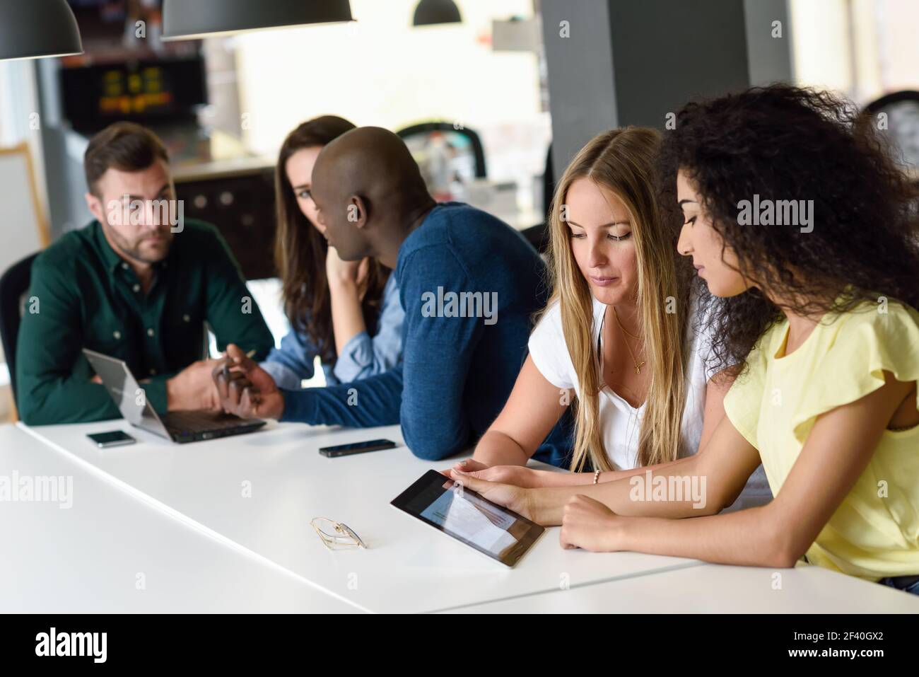 Fünf junge Menschen, die mit Tablet und Laptop auf dem weißen Schreibtisch studieren. Schöne Frauen und Männer arbeiten zusammen tragen legere Kleidung. Multiethnische Gruppe.. Multiethnische Gruppe junger Menschen, die mit einem Laptop studieren Stockfoto