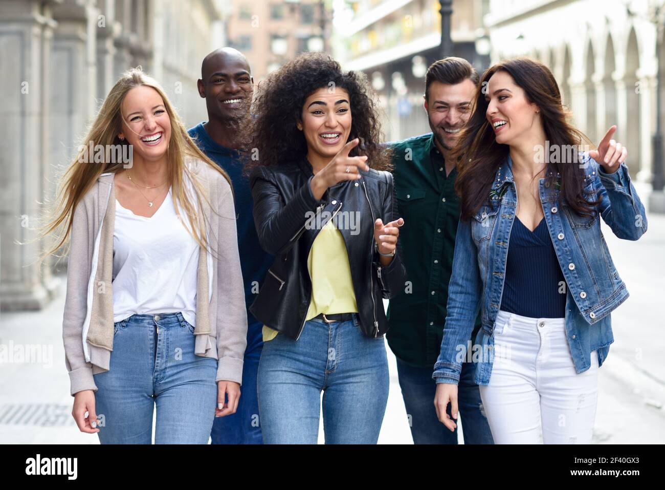 Multi-ethnische Gruppe von jungen Menschen Spaß zusammen im Freien im städtischen Hintergrund. Gruppe von Menschen zu Fuß zusammen mit dem Finger zeigen. Gruppe von Freunden, die gemeinsam Spaß im Freien haben Stockfoto