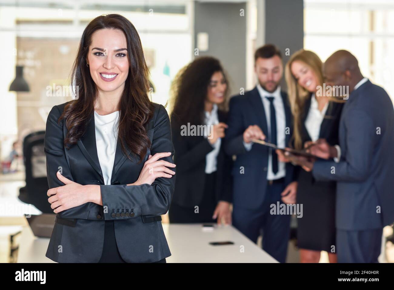 Geschäftsfrau Leader bei Kamera schaut in modernen Büro mit multi-ethnischen Geschäftsleute, die im Hintergrund arbeiten. Teamwork Konzept. Kaukasische Frau. Stockfoto