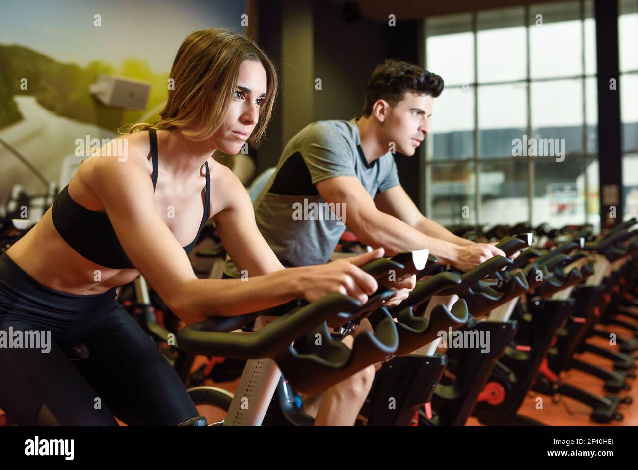 Junge Mann und Frau Radfahren in der Turnhalle, Training Beine tun Cardio-Training Radfahren Fahrräder. Zwei Personen in einer Cyclo Indoor Klasse tragen Sportkleidung. Paar in einer Cyclo-Indoor-Klasse tragen Sportkleidung. Stockfoto