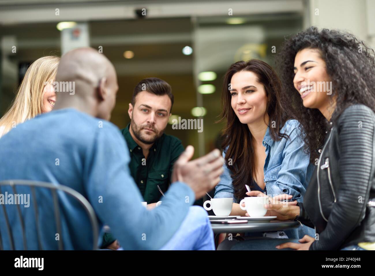 Multirassische Gruppe von fünf Freunden mit einem Kaffee zusammen. Drei Frauen und zwei Männer im Café, reden, lachen und genießen ihre Zeit. Lifestyle- und Freundschaftskonzepte mit echten Menschen-Modellen. Multirassische Gruppe von fünf Freunden mit einem Kaffee zusammen Stockfoto