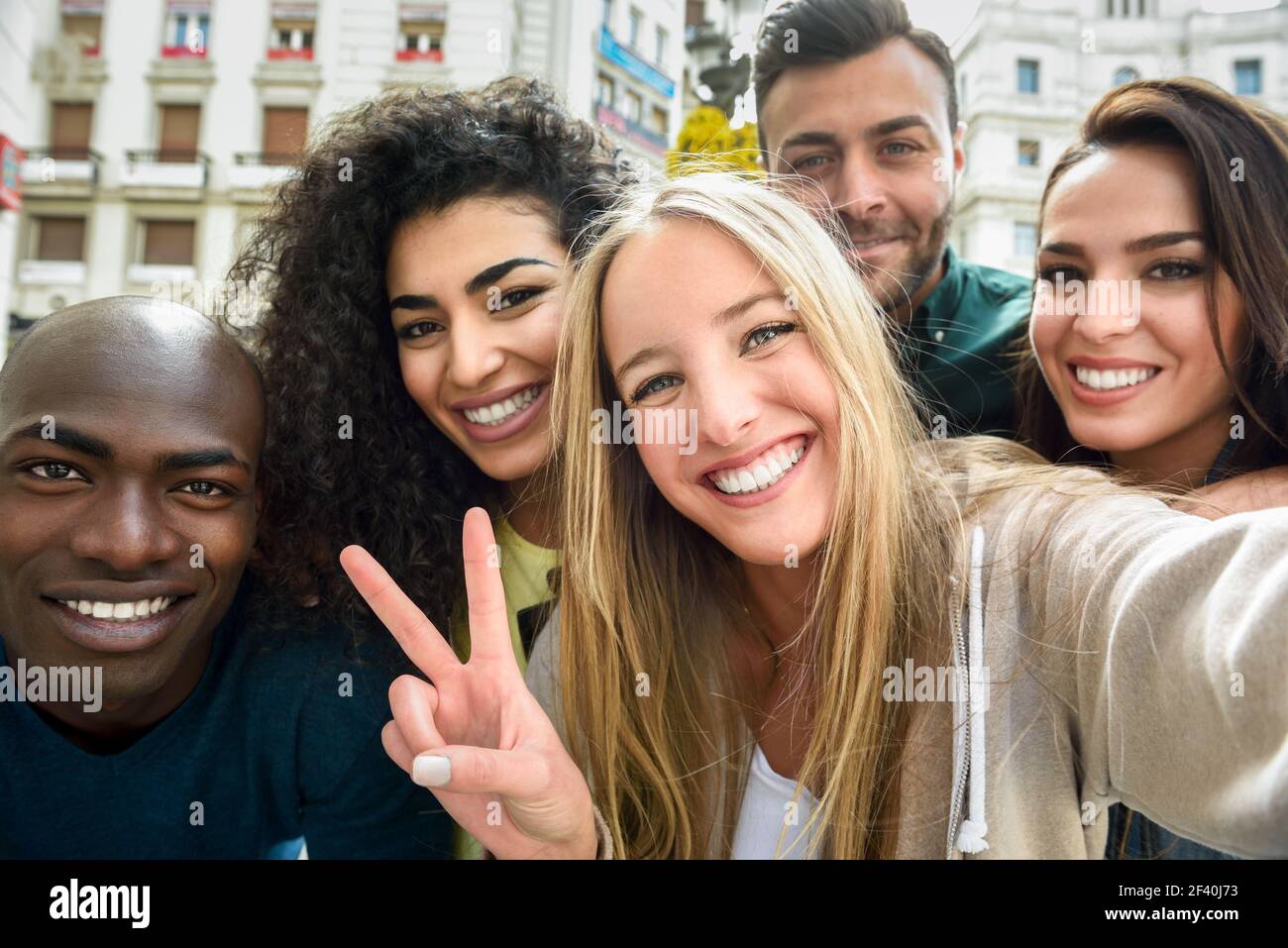 Multirassische Gruppe von Freunden, die Selfie in einer städtischen Straße mit einer blonden Frau im Vordergrund. Drei junge Frauen und zwei Männer tragen legere Kleidung. Multirassische Gruppe junger Menschen, die Selfie machen Stockfoto