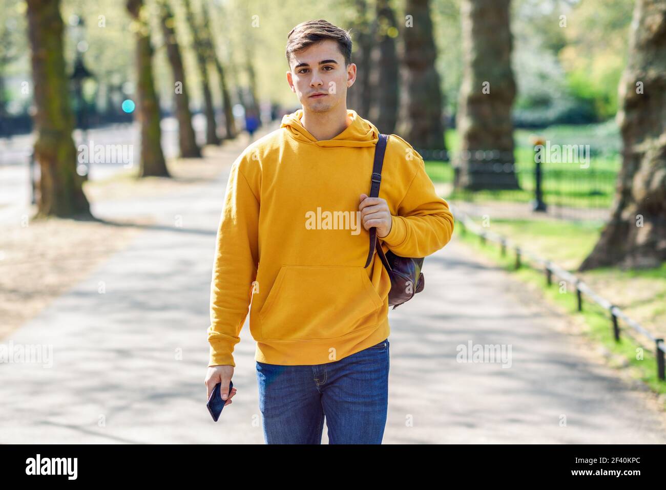 Junge Stadtmenschen mit Smartphone zu Fuß in der Straße in einem Stadtpark in London, Großbritannien.. Junger Stadtmensch mit Smartphone in einem Stadtpark in London. Stockfoto