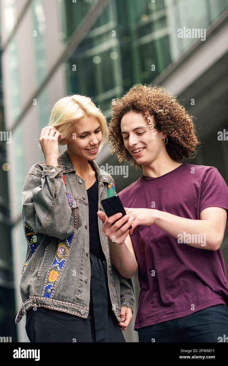 Glückliches Paar mit Smartphone im städtischen Hintergrund. Junger Mann und Frau tragen legere Kleidung in einer Londoner Straße. Glückliches Paar mit Smartphone im städtischen Hintergrund. Stockfoto
