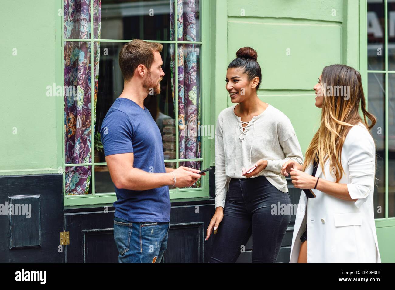 Multirassische Gruppe von Freunden im städtischen Hintergrund. Drei multiethnische Menschen reden und lächeln im Freien mit Smartphone in den Händen.. Multirassische Gruppe von Freunden, die Spaß in städtischen Hintergrund Stockfoto