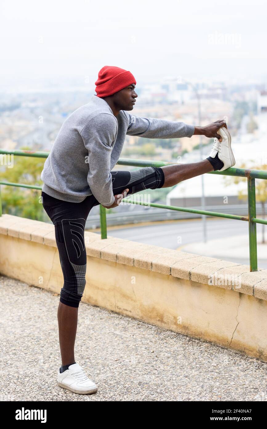 Schwarzer Mann macht Stretching vor dem Laufen im Freien. Junge männliche Ausübung mit Stadtbild im Hintergrund.. Schwarzer Mann tut Stretching vor dem Laufen im städtischen Hintergrund Stockfoto