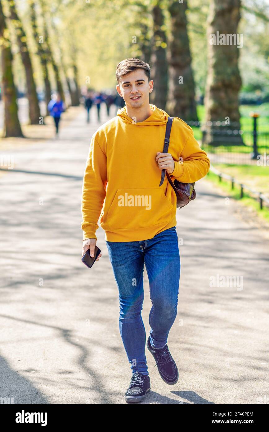 Junge Stadtmenschen mit Smartphone zu Fuß in der Straße in einem Stadtpark in London, Großbritannien.. Junger Stadtmensch mit Smartphone in einem Stadtpark in London. Stockfoto