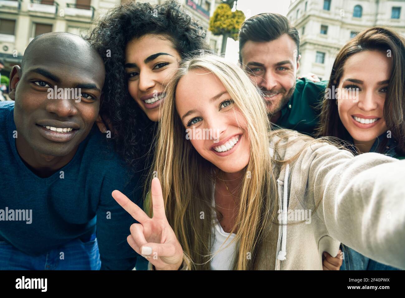 Multirassische Gruppe von Freunden, die Selfie in einer städtischen Straße mit einer blonden Frau im Vordergrund. Drei junge Frauen und zwei Männer tragen legere Kleidung. Multirassische Gruppe junger Menschen, die Selfie machen Stockfoto