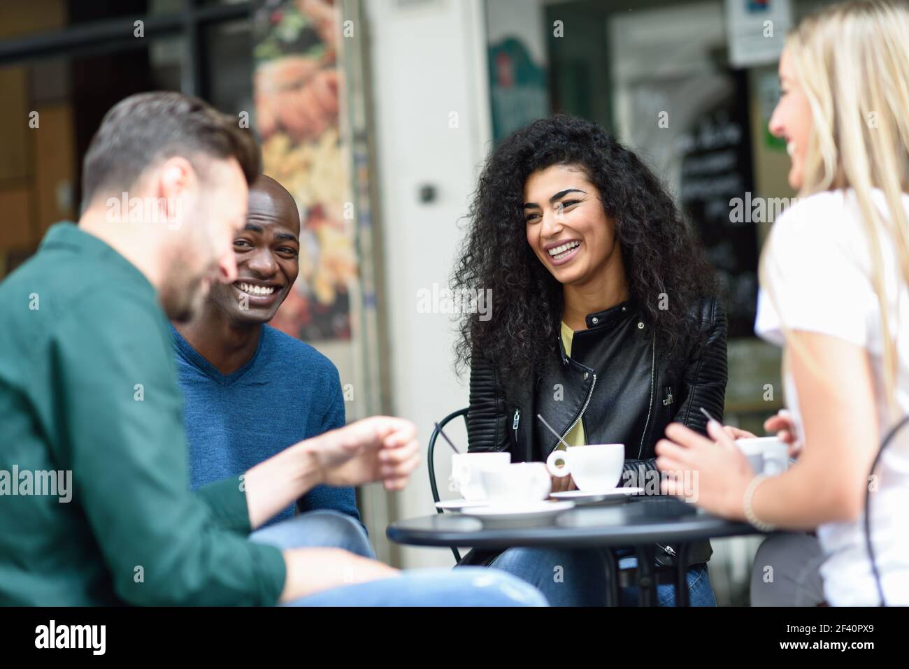 Multirassische Gruppe von vier Freunden mit einem Kaffee zusammen. Zwei Frauen und zwei Männer im Café, reden, lachen und genießen ihre Zeit.. Multirassische Gruppe von vier Freunden mit einem Kaffee zusammen Stockfoto