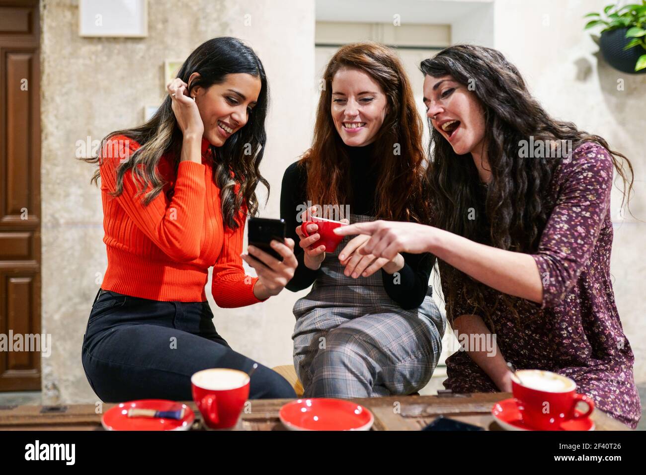 Multiethnische Gruppe von drei glücklichen Freundinnen suchen auf ein Smartphone in einer Café-Bar.. Eine Gruppe von drei glücklichen Freunden trinkt Kaffee in einer Café-Bar. Stockfoto