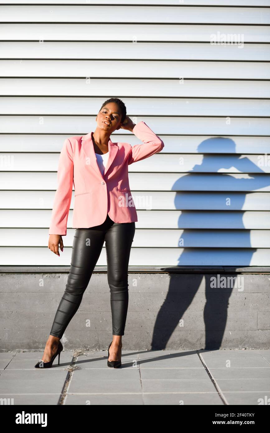 Schwarze Frau, Modell der Mode, auf der Stadtmauer stehend. afroamerikanische Frauenanzug mit rosa Jacke mit Sonnenuntergang Licht.. Schwarze Frau, Modell der Mode, auf der Stadtmauer stehend Stockfoto