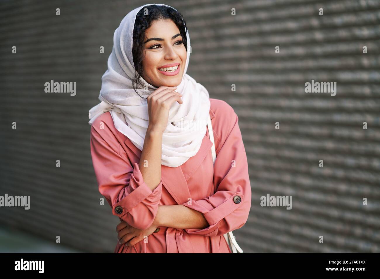 Glückliche arabische Frau trägt Hijab Kopftuch zu Fuß in der Innenstadt. Muslimische Frau im städtischen Hintergrund. Junge muslimische Frau trägt Hijab Kopftuch zu Fuß in der Innenstadt. Stockfoto