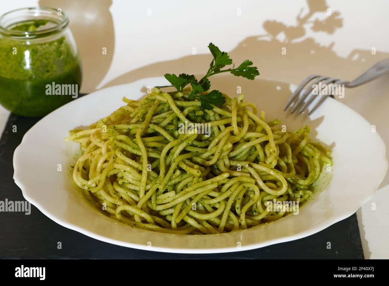 Spaghetti mit Pesto-Sauce und einem Petersilienblatt in einem Teller und  ein Glas Pesto Sauce Stockfotografie - Alamy