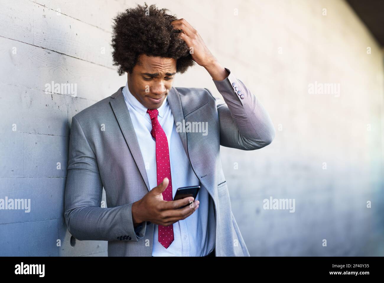 Besorgt Black Geschäftsmann mit seinem Smartphone in der Nähe eines Bürogebäudes. Mann mit afro Haar.. Besorgt schwarzen Geschäftsmann mit seinem Smartphone im Freien. Stockfoto
