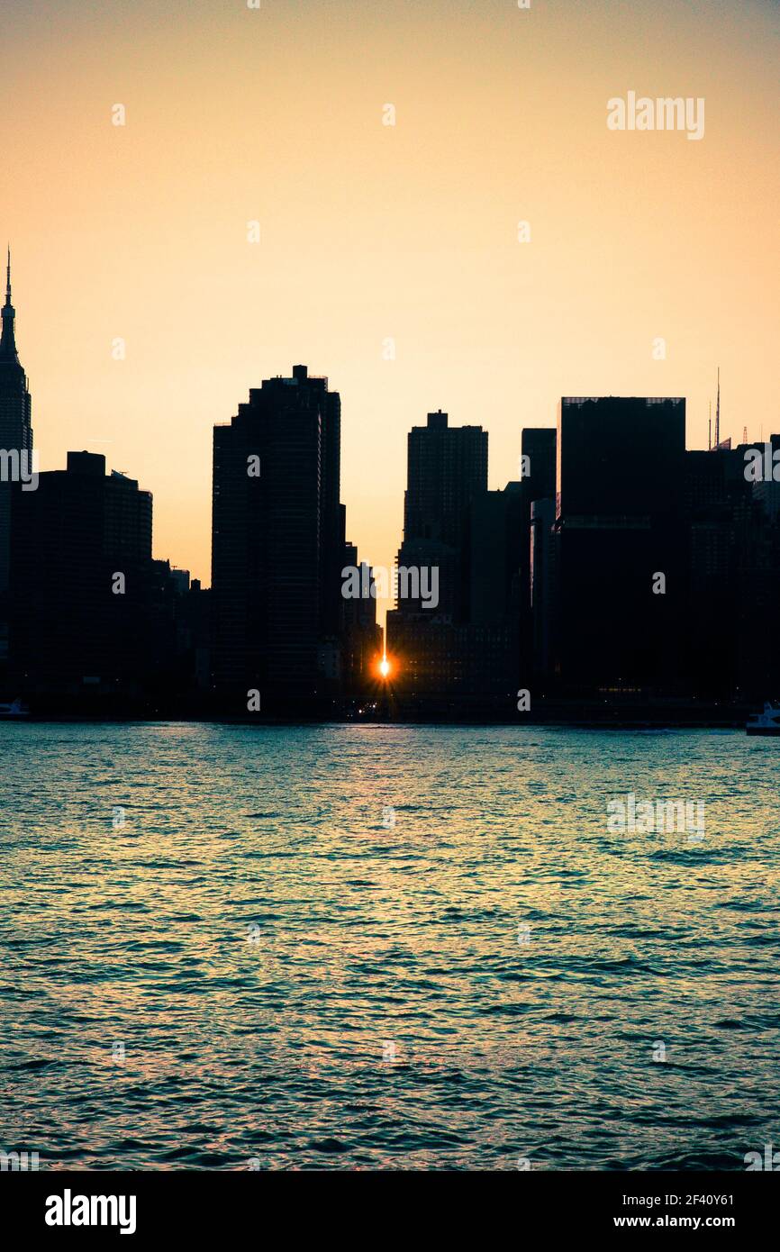Manhattan Manhattanhenge New York City Skyline bei Sonnenuntergang mit Sonnenlicht Hintergrundbeleuchtung und zwischen den Gebäuden gesehen. Stockfoto