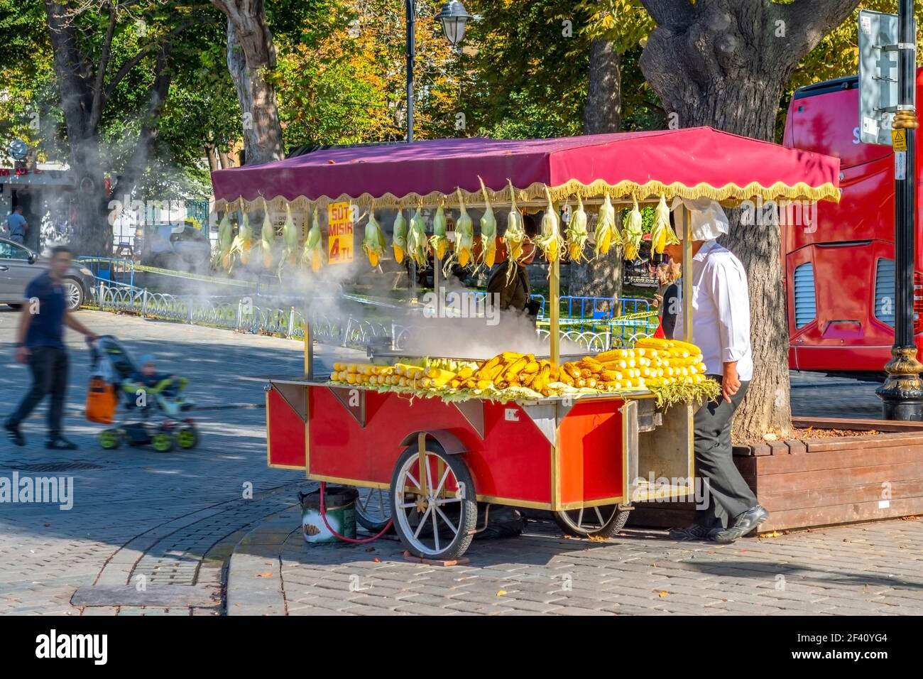 Ein Anbieter verkauft frisch gekochte Maiskolben im Stadtteil Sultanahmet Square Bezirk von Istanbul Türkei, wie ein Mann mit einem Kinderwagen vorbei. Stockfoto