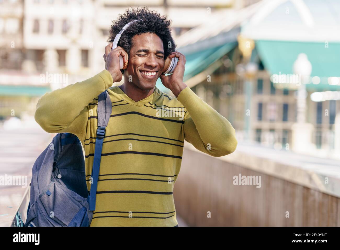 Kubanischer schwarzer Mann mit afro Haar Musik hören mit kabellosen Kopfhörern Sightseeing in Granada, Andalusien, Spanien.. Schwarzer Mann, der Musik mit kabellosen Kopfhörern bei der Besichtigung von Granada hört Stockfoto