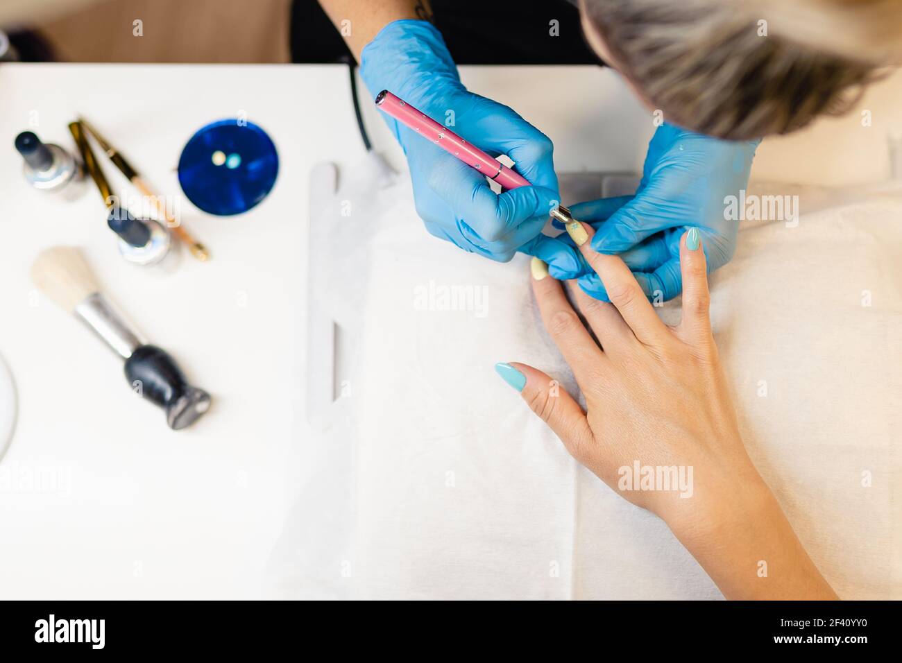 Nahaufnahme der Kosmetikerin, die ihre Klienten mit blauen und gelben Nagellacken in einem Beauty-Center malt. Nahaufnahme der Kosmetikerin, die ihre Klienten mit blauen und gelben Nagellacken bemalt. Stockfoto