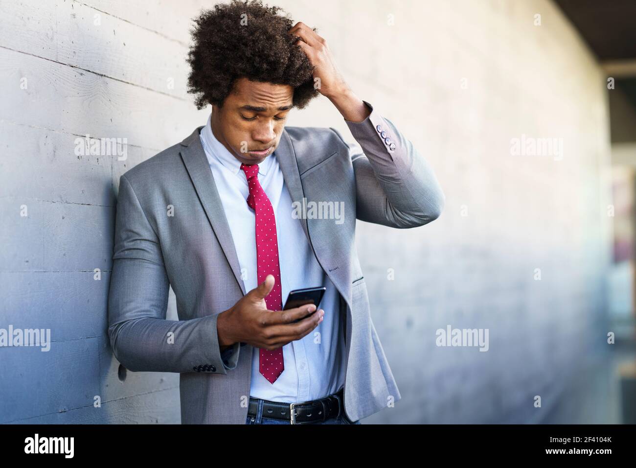 Besorgt Black Geschäftsmann mit seinem Smartphone in der Nähe eines Bürogebäudes. Mann mit afro Haar.. Besorgt schwarzen Geschäftsmann mit seinem Smartphone im Freien. Stockfoto