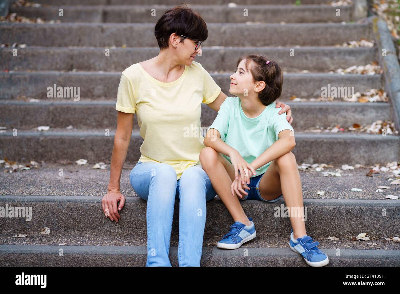 Mutter und Tochter mittleren Alters sitzen auf der Straße auf städtischen Treppen. Mutter und Tochter mittleren Alters sitzen auf der Straße Stockfoto