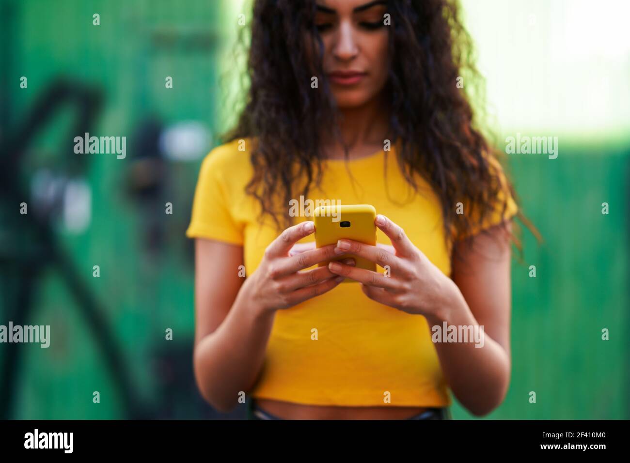 Junge arabische Frau SMS eine SMS mit ihrem Smartphone gegen grüne Stadtmauer.. Junge arabische Frau, die mit ihrem Smartphone auf der Straße unterwegs ist Stockfoto