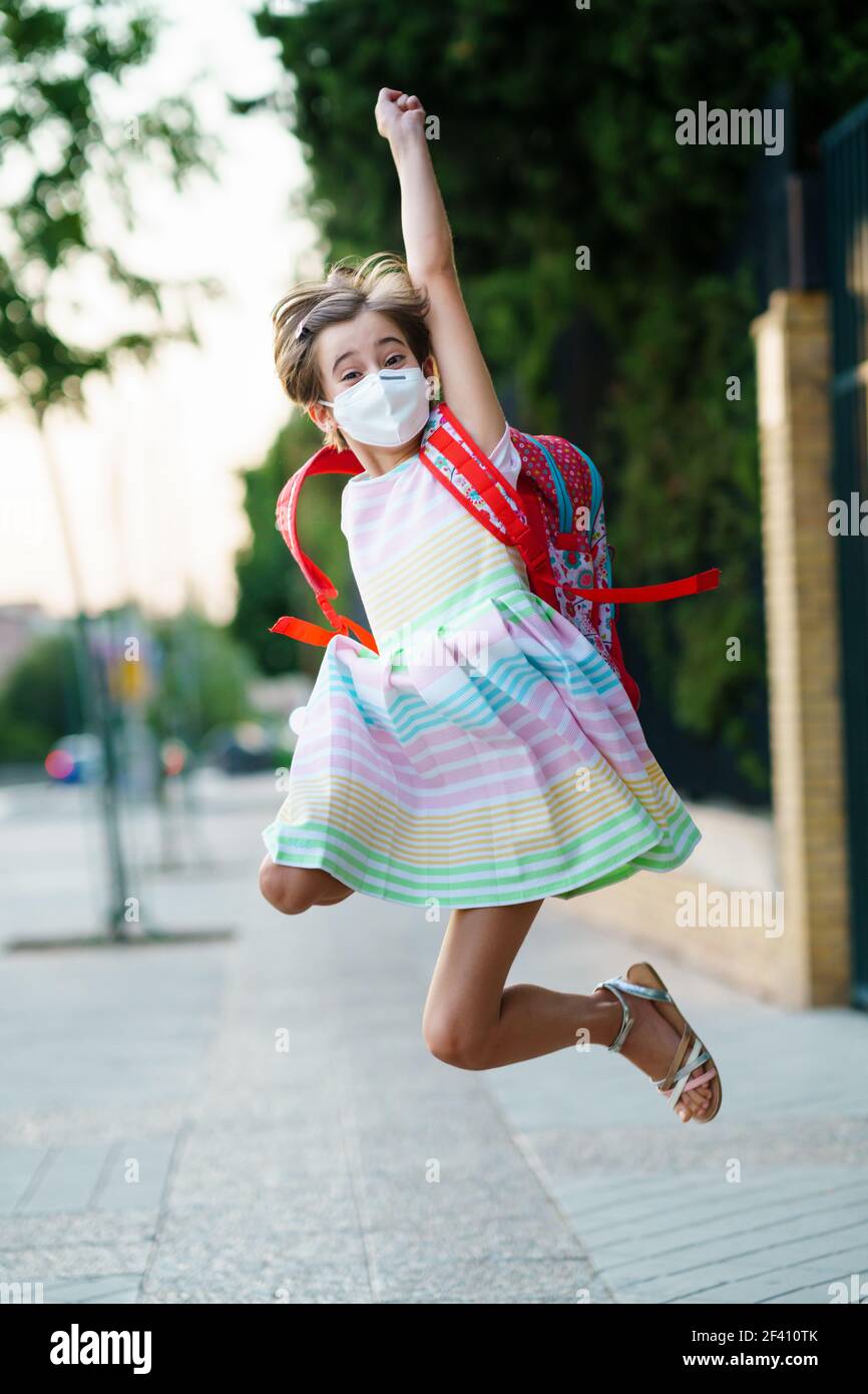 Mädchen trägt eine Maske macht einen Sprung vor Freude an der Rückkehr in die Schule. Zurück zur Schule Konzept.. Mädchen trägt eine Maske macht einen Sprung vor Freude an der Rückkehr in die Schule. Stockfoto