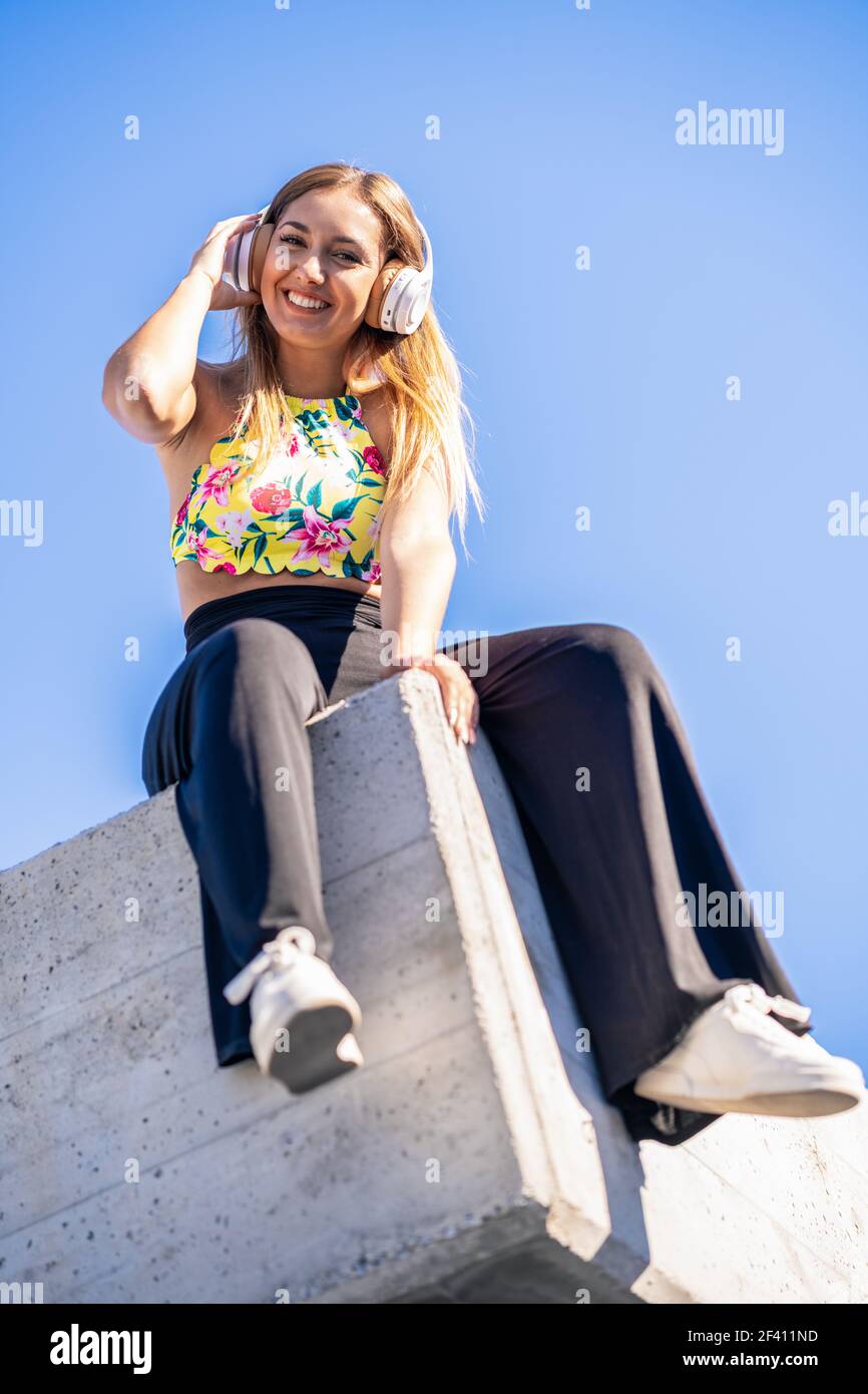 Junge Frau, die Kamera mit Kopfhörern gegen blauen Himmel.. Junge Frau, die die Kamera mit Kopfhörern anschaut Stockfoto
