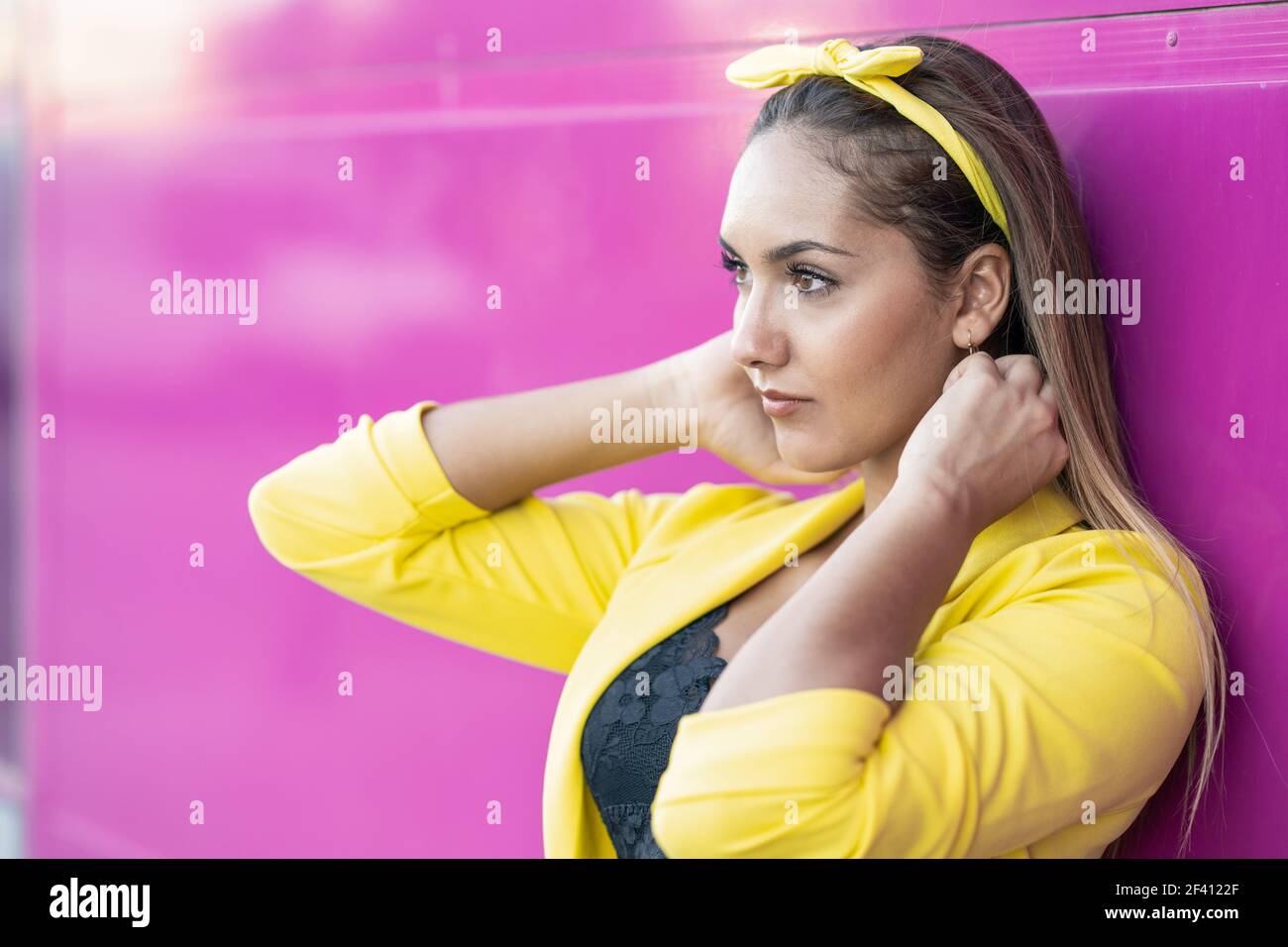 Junge Frau mit gelber Jacke und Stirnband, in der Nähe einer städtischen lila Wand. Junge Frau mit gelber Jacke und Stirnband Stockfoto