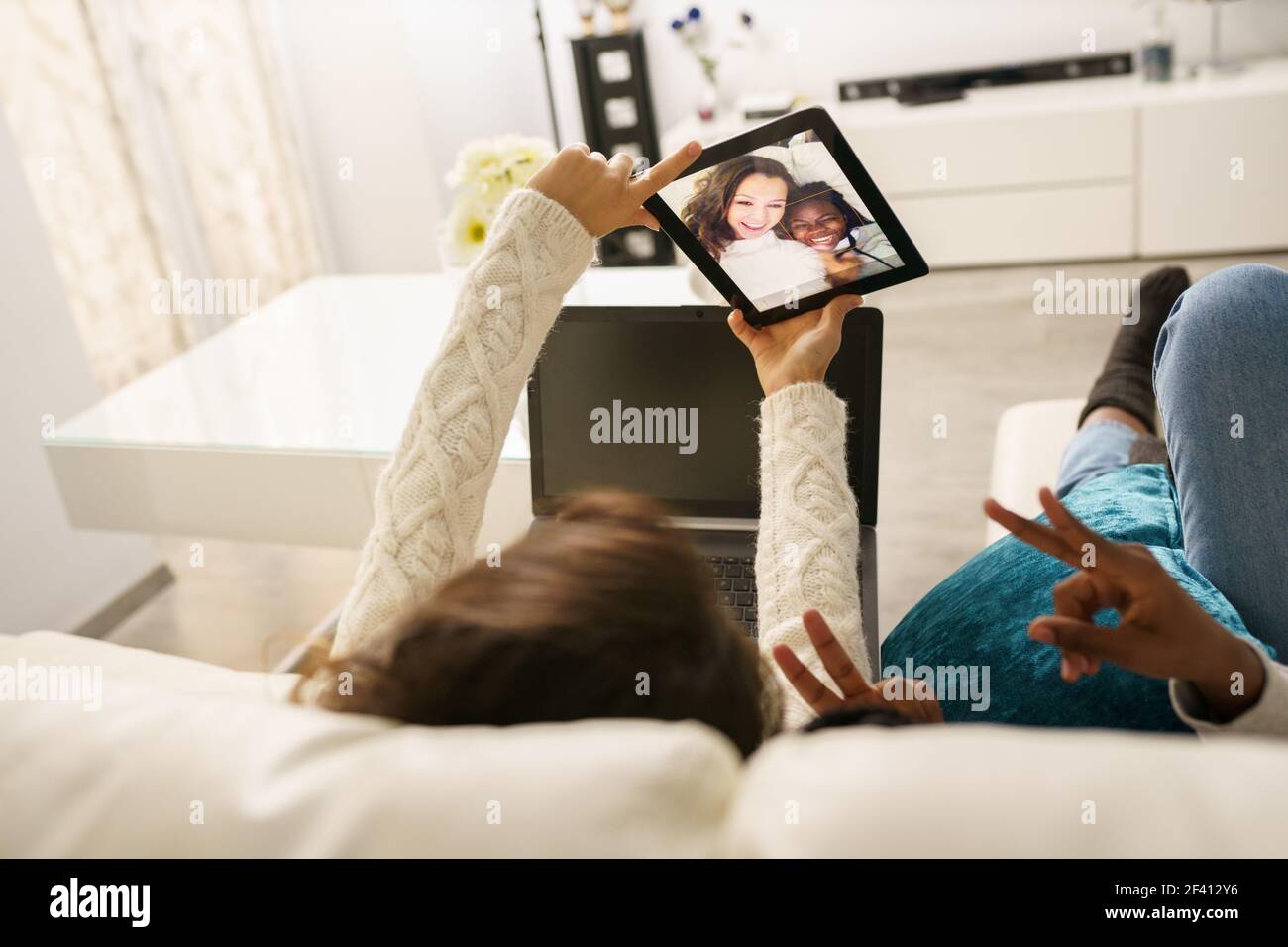 Zwei Freundinnen machen ein Selfie mit einem digitalen Tablet, das zu Hause auf der Couch sitzt. Multiethnische Frauen... Zwei Freundinnen machen ein Selfie mit einem digitalen Tablet, das zu Hause auf der Couch sitzt. Stockfoto