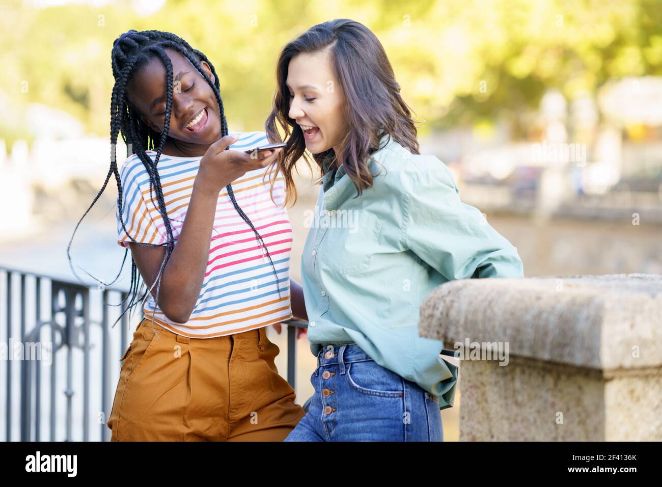 Zwei Freundinnen, die eine Sprachnotiz mit dem Smartphone im Freien aufnehmen. Multiethnische Freunde... Zwei Freundinnen, die gemeinsam auf der Straße Spaß haben. Multiethnische Freunde. Stockfoto