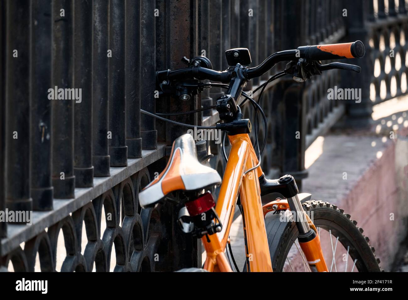 Winkel Blick auf moderne Stil Mountain Bike orange Farbe durch den Zaun in der Stadt Straße im alten Teil der Stadt gesperrt. Mountain Bike durch den Zaun in der Stadt Straße in der Stadt gesperrt Stockfoto