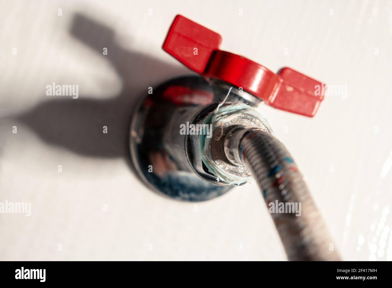 Rotes Ventil auf flexiblem Rohr im Badezimmer, Hausreparaturkonzept Stockfoto