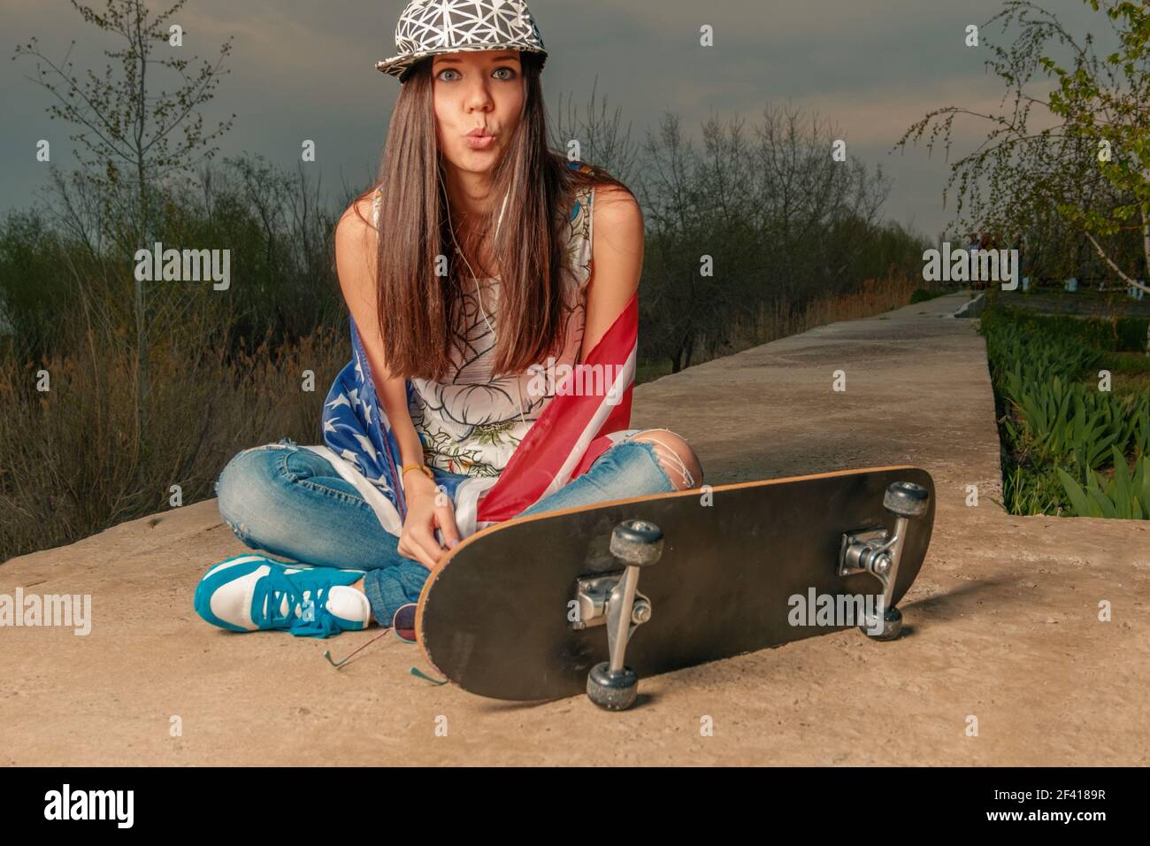 Skater Mädchen sitzt auf Zement Lane mit ihrem Skateboard drapiert in US-Flagge instagram Farbe getönten. Skater Mädchen sitzt auf Zement Lane mit ihrem Skateboard drapiert in US-Flagge Stockfoto