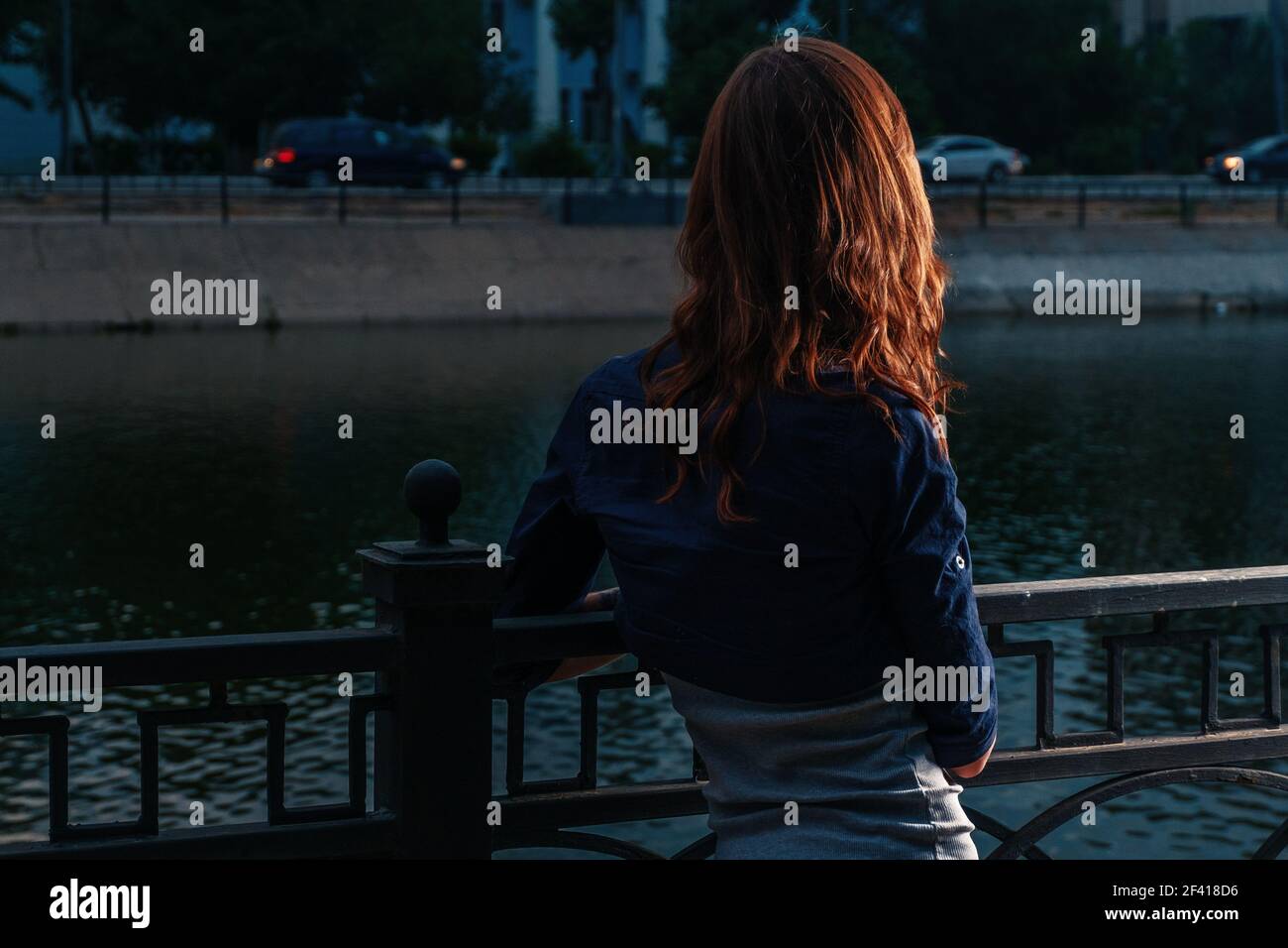Einsames Wochenende. Rothaarige Mädchen Blick auf Nacht Fluss im Stadtpark mit Highlight auf ihre hübschen Ingwer Haar.. Einsames Wochenende. Rothaarige Mädchen Blick auf Nacht Fluss im Stadtpark Stockfoto