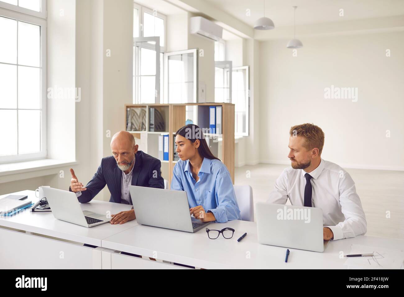 Senior Colleague zeigt auf einen Laptop und berät junge Büroangestellte bei einem neuen Projekt. Stockfoto