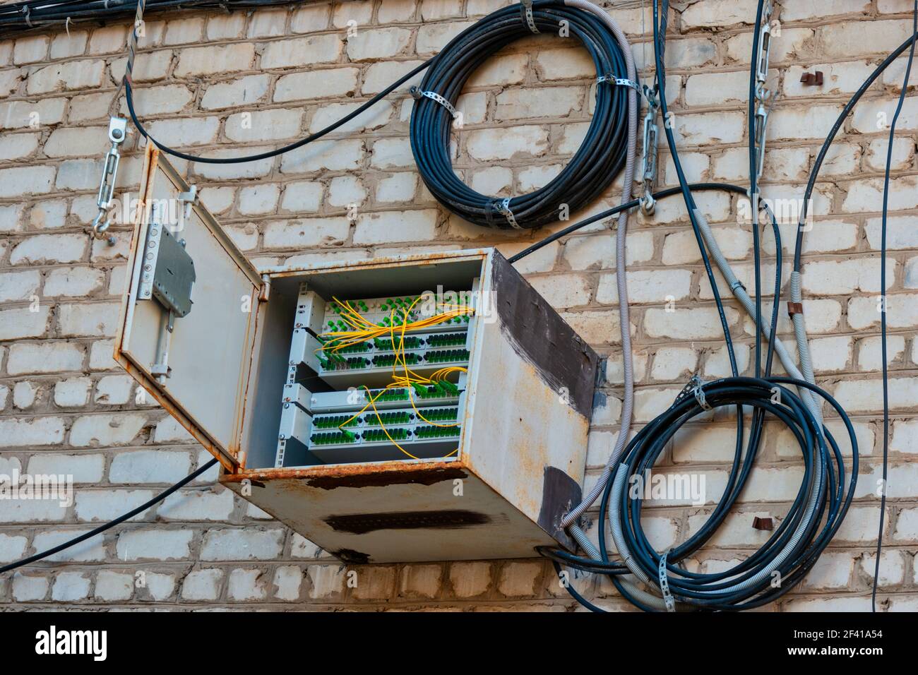 Witterungsversiegelte Box mit Glasfaser-Schalter an der Wand des Wohngebäudes und Spulen von geschützten Drähten in der Nähe hängen platziert. Witterungsversiegelte Box mit Glasfaser-Schalter an der Wand des Wohngebäudes platziert Stockfoto