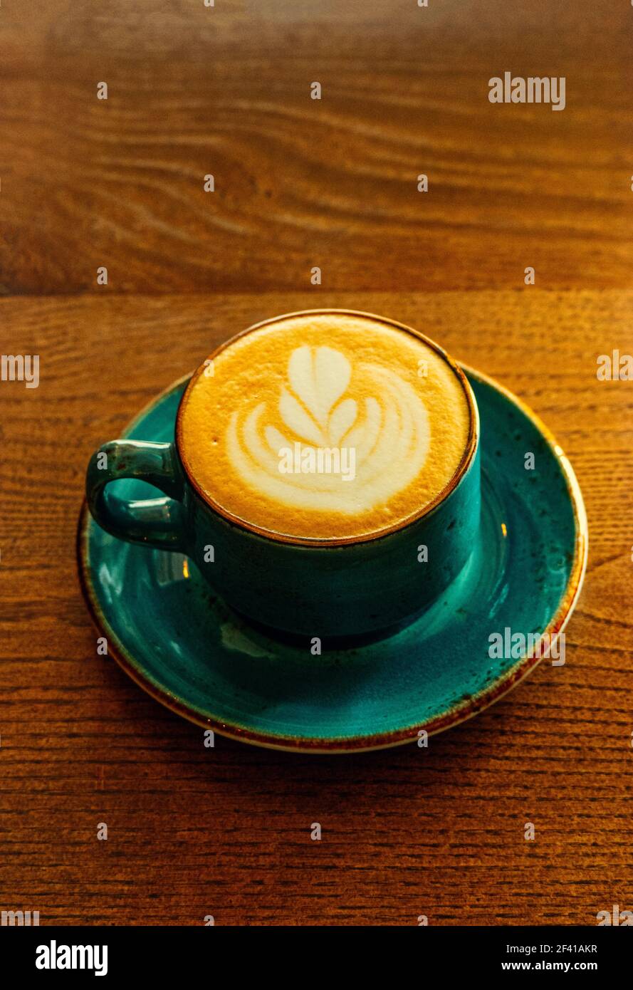 Vertikales Bild der grünen Farbe Kaffeetasse voll Cappuccino Kaffee steht auf der Tischplatte, inage mit viel Kopieplatz.. Vertikales Bild der grünen Kaffeetasse voll Cappuccino Kaffee steht auf der Tischplatte, inage mit viel Kopieplatz. Stockfoto