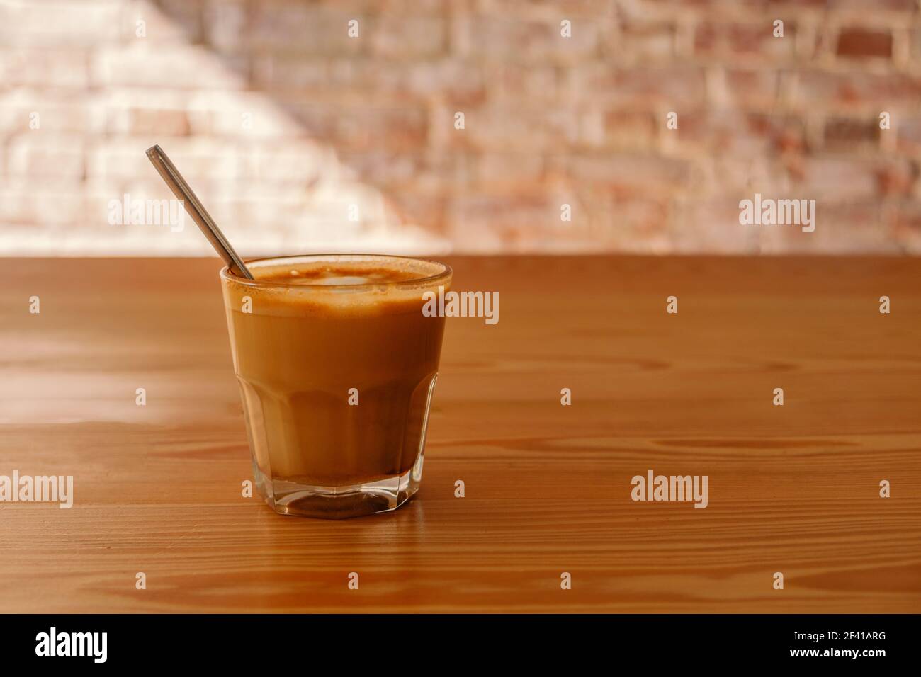 Flacher weißer Kaffee aus transparentem Glas auf Holztisch. Es ist Espresso-basierte Kaffee-Getränk, bestehend aus Espresso mit Mikroschaum gedämpfter Milch mit kleinen Blasen mit einer glänzenden oder samtigen Konsistenz.. Flacher weißer Kaffee aus transparentem Glas auf dem Tisch im Café. Es ist ein Espresso-basiertes Kaffeegetränk, bestehend aus Espresso mit gedämpfter Mikroschaum-Milch mit feinen Blasen mit einer glänzenden oder samtigen Konsistenz Stockfoto