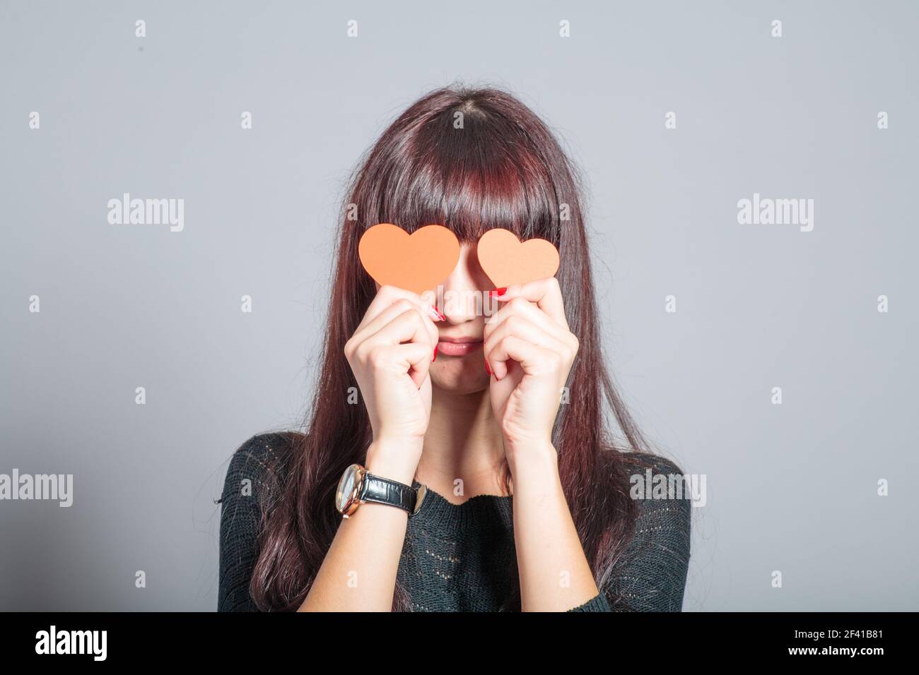 Braune Frau bedeckt ihre Augen mit zwei Papierherzen Stockfoto