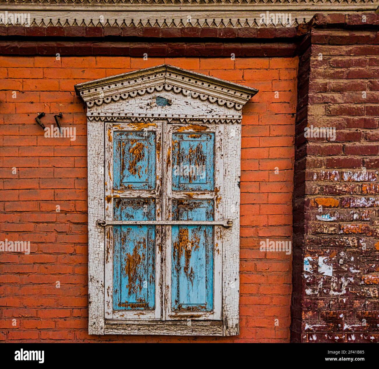 Ein altes geschnitztes Holzfenster mit verschlossenen Fensterläden Wand eines Ziegelhauses Stockfoto