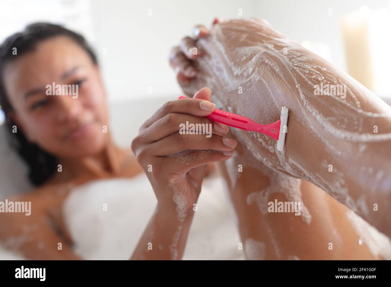 afroamerikanische Frau rasieren ihre Beine in der Badewanne im Badezimmer Stockfoto