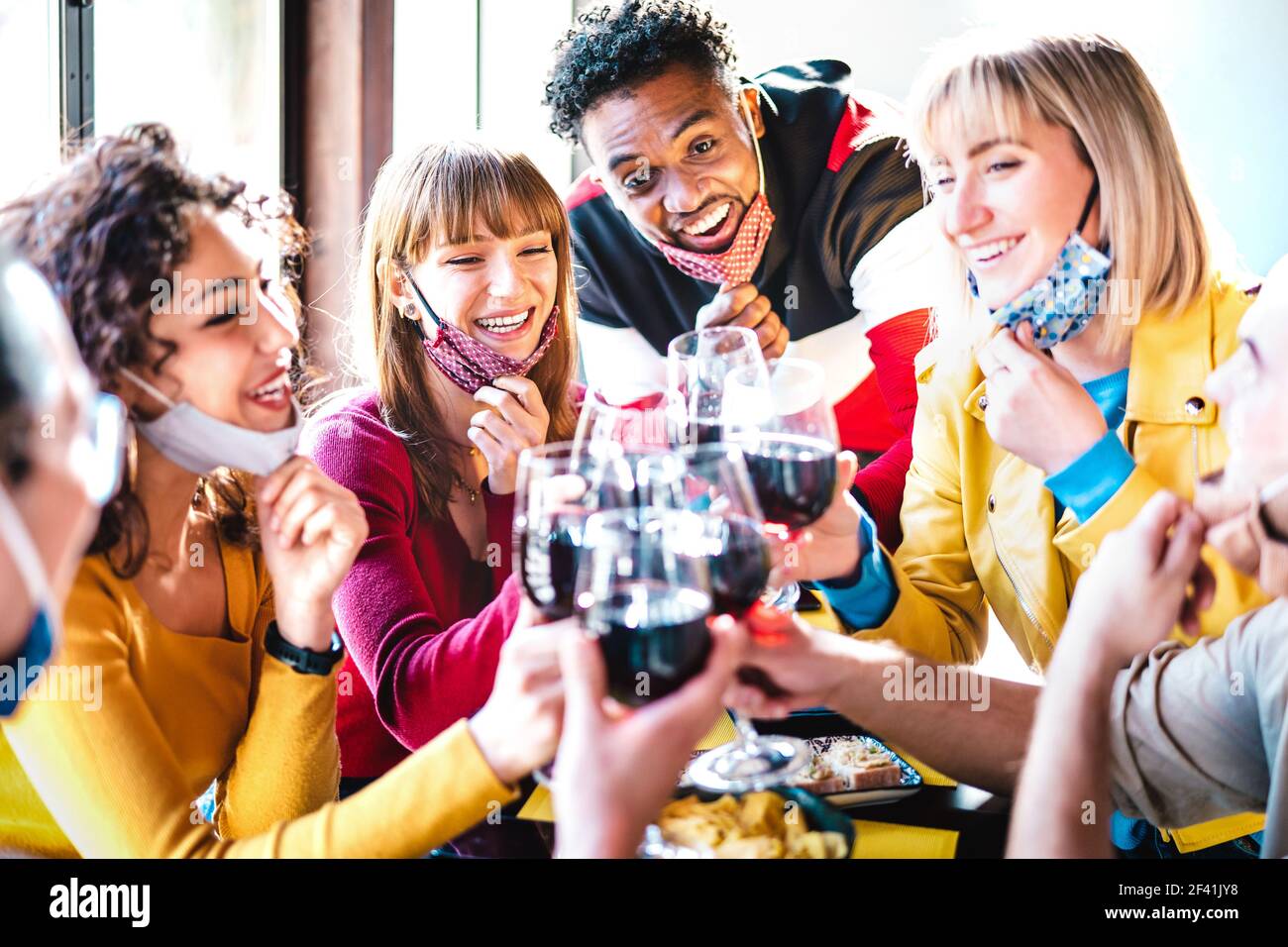 Multirassische Freunde, die Rotwein in der Restaurantbar toasten und offen tragen Gesichtsmaske - Neue normale Lebensstil Konzept mit glücklich Menschen, die Spaß zusammen haben Stockfoto