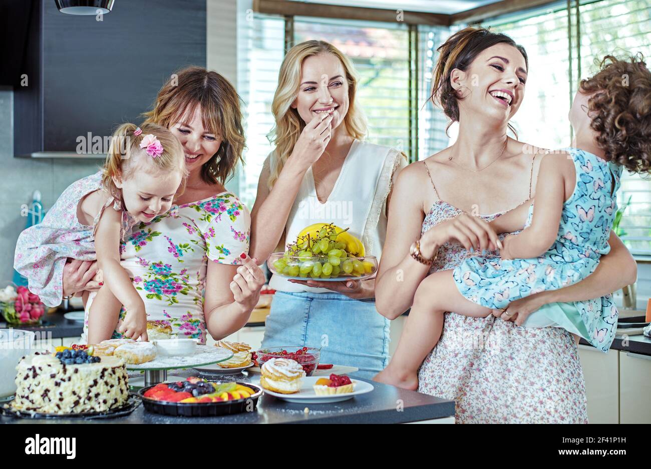 Fröhliche junge Frauen essen Kuchen und Süßigkeiten mit ihren Kindern Stockfoto