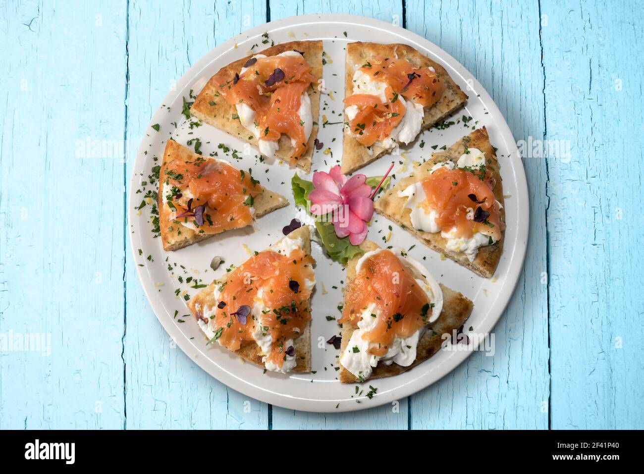Pizza mit Lachs und Mozzarella burrata Käse, sechs Scheiben in weißem Teller auf hellblauem Holzbrett Hintergrund, flach in Draufsicht Stockfoto